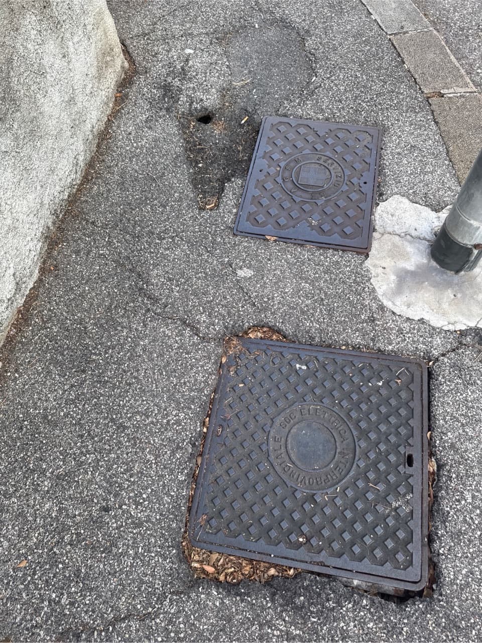 Si osserva un buco sul marciapiede accanto a un tombino, che